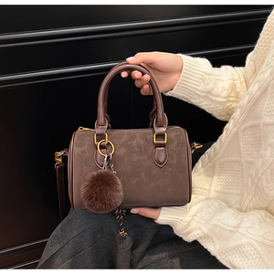 Détail du sac Boston marron foncé avec pompon en fourrure et finitions métalliques dorées