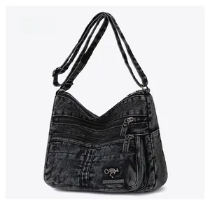 Detail of gray denim crossbody bag featuring multi-layer zippers and metal logo