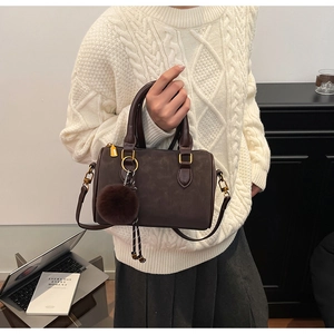 Détail d'un sac Boston marron foncé en daim avec boucles dorées et pompon décoratif