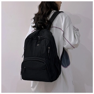 Detail view of black nylon backpack showing multi-pocket structure and metal logo