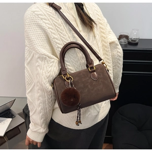 Détail d'un sac Boston marron café vintage en daim avec un pendentif pompon doux
