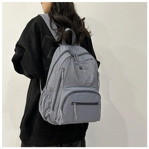 Detail of grey-blue nylon backpack showing multiple utility pockets and drawstring zippers