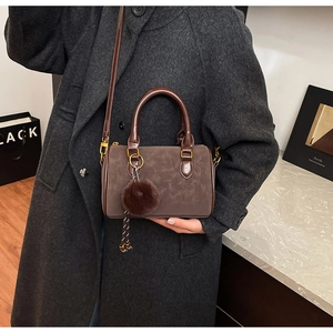 Détail du sac Boston en daim marron foncé avec ferrures dorées et pompon doux