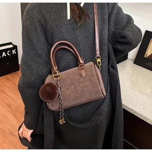 Vue détaillée du sac Boston en daim marron foncé avec pompon et pendentif métallique M