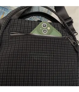 Close-up of the front zipper pocket on black checkered nylon bag with a phone inside