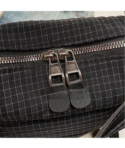 Detail view of durable metal dual zippers on a black checkered casual crossbody bag