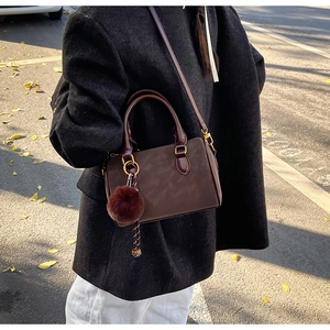 Détail du sac Boston en daim marron foncé avec pompon en peluche et bandoulière