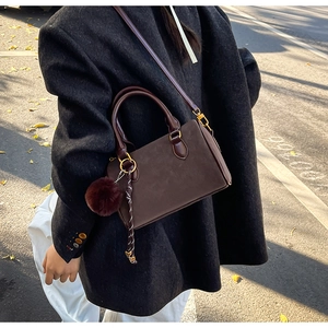 Détail du sac bandoulière en daim marron foncé avec pompon en peluche et boucles dorées