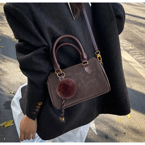 Détail d'un sac à bandoulière en cuir marron foncé avec pompon et manteau d'hiver