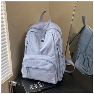 Detail of light blue nylon backpack with multiple zipper pockets on a black surface
