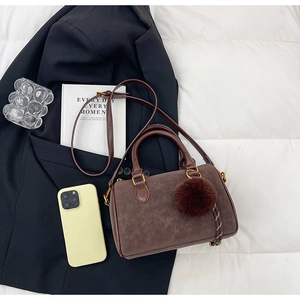 Détail d'un sac polochon marron en daim avec pompon pelucheux sur un blazer noir