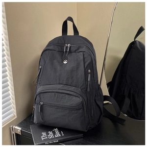 Detailed view of black nylon backpack with multi-pocket design on a wooden desk