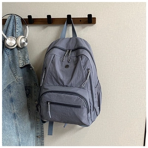 Detail of grey-blue nylon backpack with multiple zipper pockets hanging on a wall