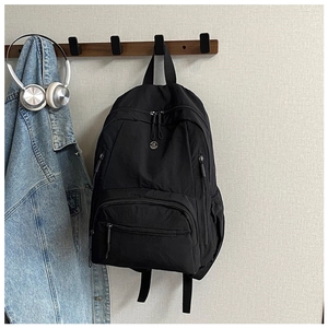 Detail of black nylon backpack with multiple zipper pockets and circular logo