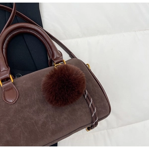 Gros plan du sac boston en daim marron avec poignée en cuir et breloque pompon
