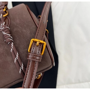 Détail du sac en cuir marron avec boucle dorée réglable et accents de corde tressée
