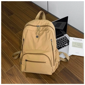 Detail of a khaki nylon travel backpack with multiple pockets on a wooden floor
