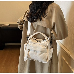 Detail of ivory nylon crossbody bag showing ribbed texture and functional side pockets