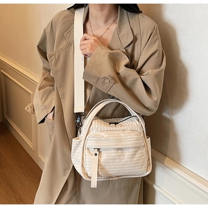 Detail of beige striped nylon crossbody bag showing the front zipper pocket and strap