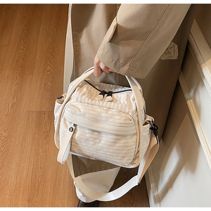 Close-up of cream nylon crossbody bag with textured stripe detail and multiple pockets
