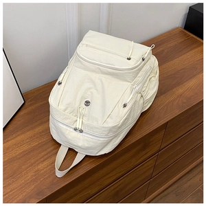 Detail of cream nylon multi-pocket backpack showing zippers and textile handle