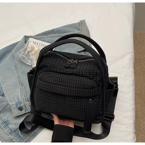 Detailed view of black plaid nylon crossbody bag on white linen with lifestyle props
