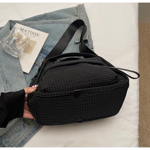 Detail of grey checkered nylon messenger bag shown with artistic books in a minimalist setting