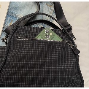 Detail of front zipper pocket on black plaid nylon crossbody bag with smartphone inside