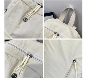 Detail of beige nylon backpack showing double metal zippers and circular fashion badge