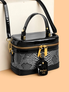 Detail of box handbag featuring black patent leather and snakeskin texture with gold hardware