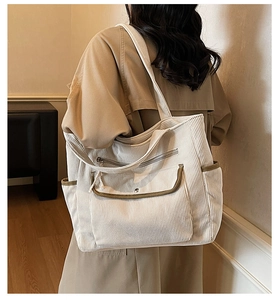 Detail of corduroy tote bag showing multiple pockets and textured fabric on model