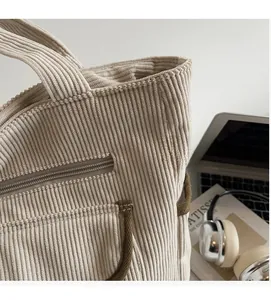 Detail of beige corduroy tote bag showing soft ribbed texture and brown piping trim