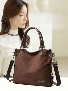 Close-up of brown suede tote bag with adjustable strap and brand label on white knitwear