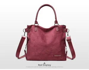 Detail view of red suede tote bag showing texture, brand name, and adjustable strap