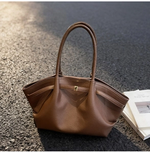 Détail du sac cabas en cuir grainé marron avec boucle dorée sur un sol en asphalte