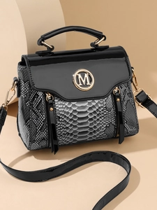 Detail of black crossbody bag with faux snake skin texture and metal M logo hardware