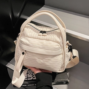 Minimalist cream nylon crossbody bag with adjustable strap on a book background