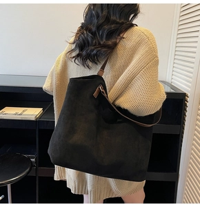 Close-up of black suede tote bag with brown leather straps worn by a model in casual knitwear