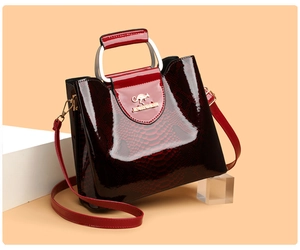 Macro detail of wine red patent leather handbag with gold kangaroo logo and embossed texture
