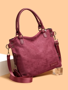 Detail of burgundy suede tote bag featuring leather brand tag and vintage bronze hardware