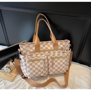 Detail of checkered tote bag with two zip pockets and adjustable strap on white bed