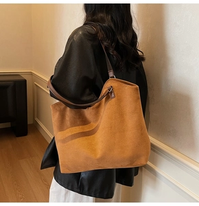 Grand sac cabas en daim marron avec bretelles en cuir, porté par un mannequin dans une pièce