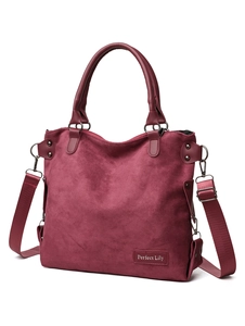 Detail of burgundy suede tote bag featuring a fabric strap and metal rivet accents