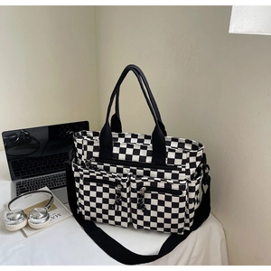 Detail of checkerboard tote bag featuring dual front zipper pockets and adjustable strap