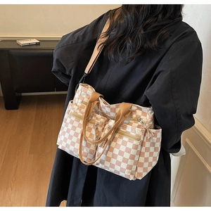 Detail view of pink checkerboard tote bag with multiple zip pockets and brown straps