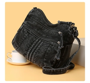 Détail d'un sac bandoulière en denim noir délavé avec poches zippées et pompons à franges