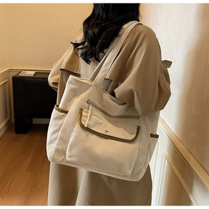 Detail of beige corduroy tote bag with olive contrast piping worn by a model