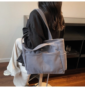 Detail of gray corduroy tote bag showing ribbed texture and dual front pockets on the strap