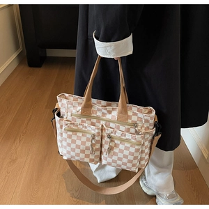 Detail of checkered tote bag showing dual zipper front pockets and wide crossbody strap