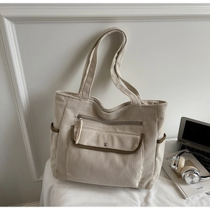Detail of beige corduroy tote bag featuring olive contrast trim and multi-pocket design